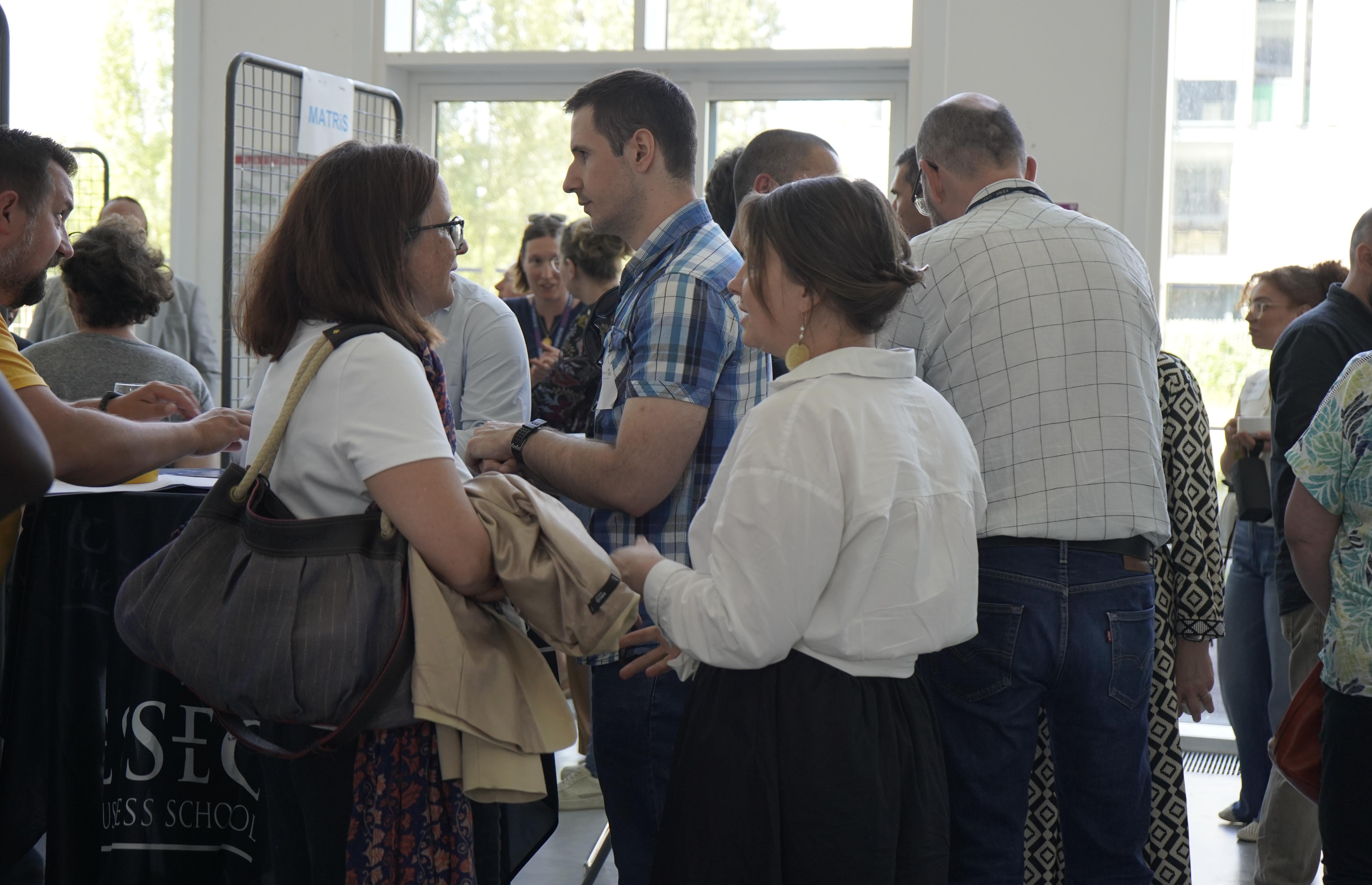 ¨hoto des participants en train de dicsuter autour des stands du forum dans le hall de la maison SHS